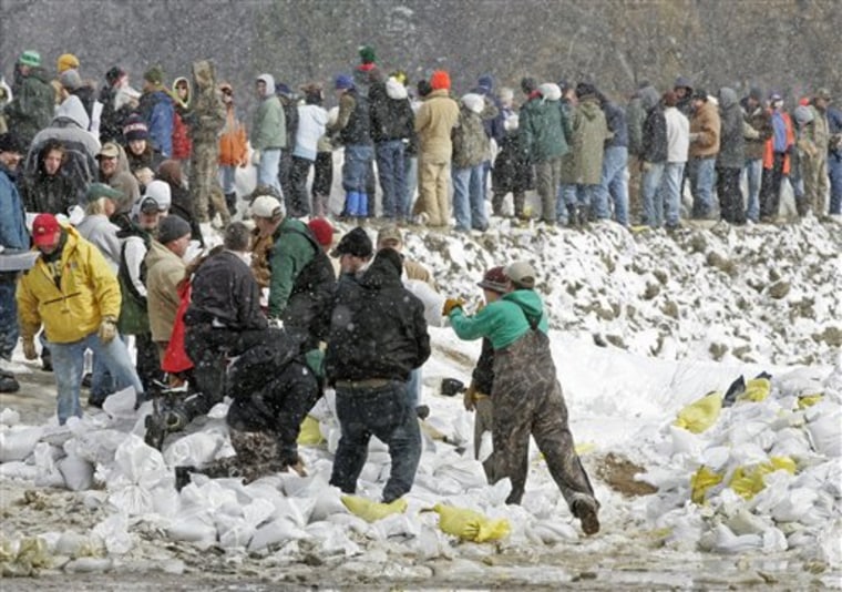 Snow flurries fall as scores of volunteers build up a dike to hold back the rising Red River flood waters in Fargo, N.D. in this March 27, 2009 file photo. During last spring's flooding, a statewide 211 number established to take calls for social services fielded more than 40,000 inquiries. Now the number may go out of business in most of the state.